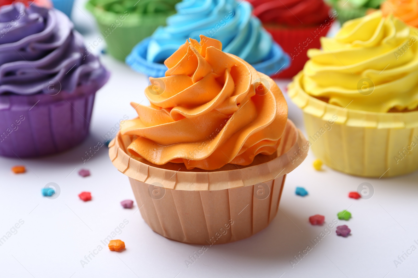 Photo of Many tasty cupcakes with bright cream and sprinkles on white background, closeup