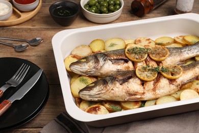 Photo of Baking tray with delicious baked sea bass fish and potatoes on wooden table