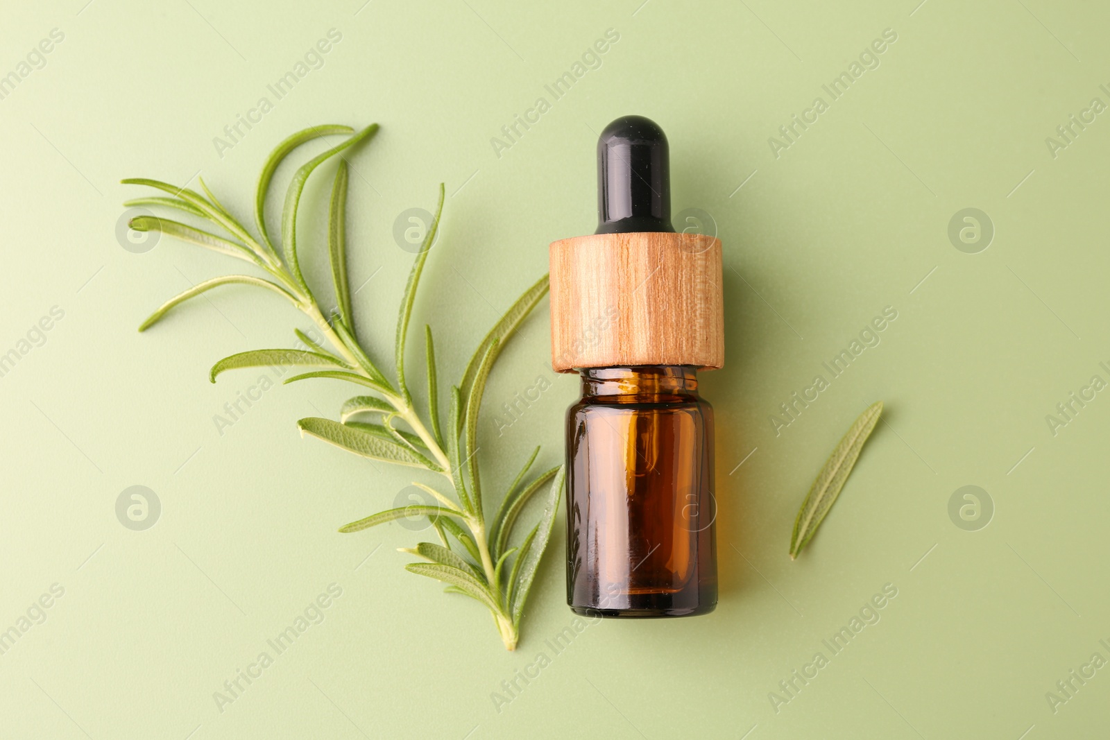 Photo of Aromatic essential oil in bottle and rosemary on green background, flat lay