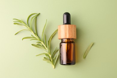 Photo of Aromatic essential oil in bottle and rosemary on green background, flat lay