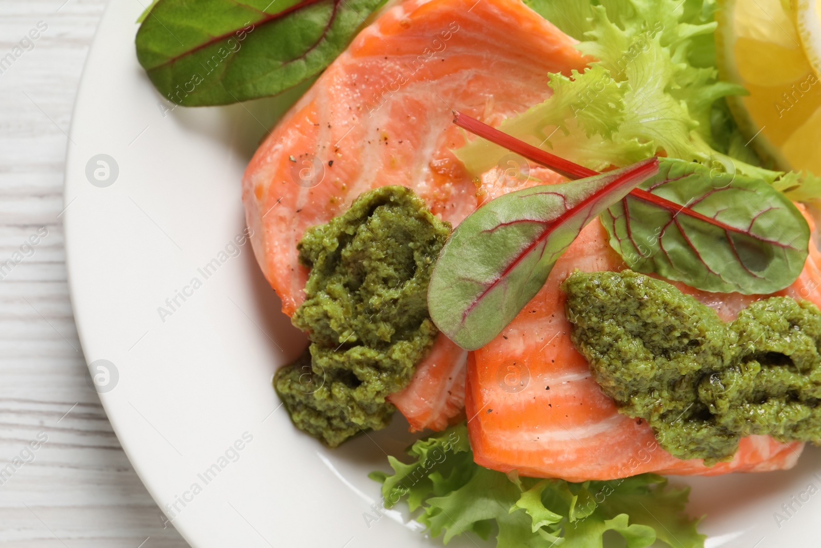 Photo of Tasty cooked salmon with pesto sauce on white wooden table, top view