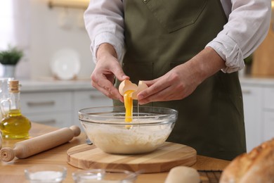 Making bread. Man putting raw egg into dough at wooden table in kitchen, closeup