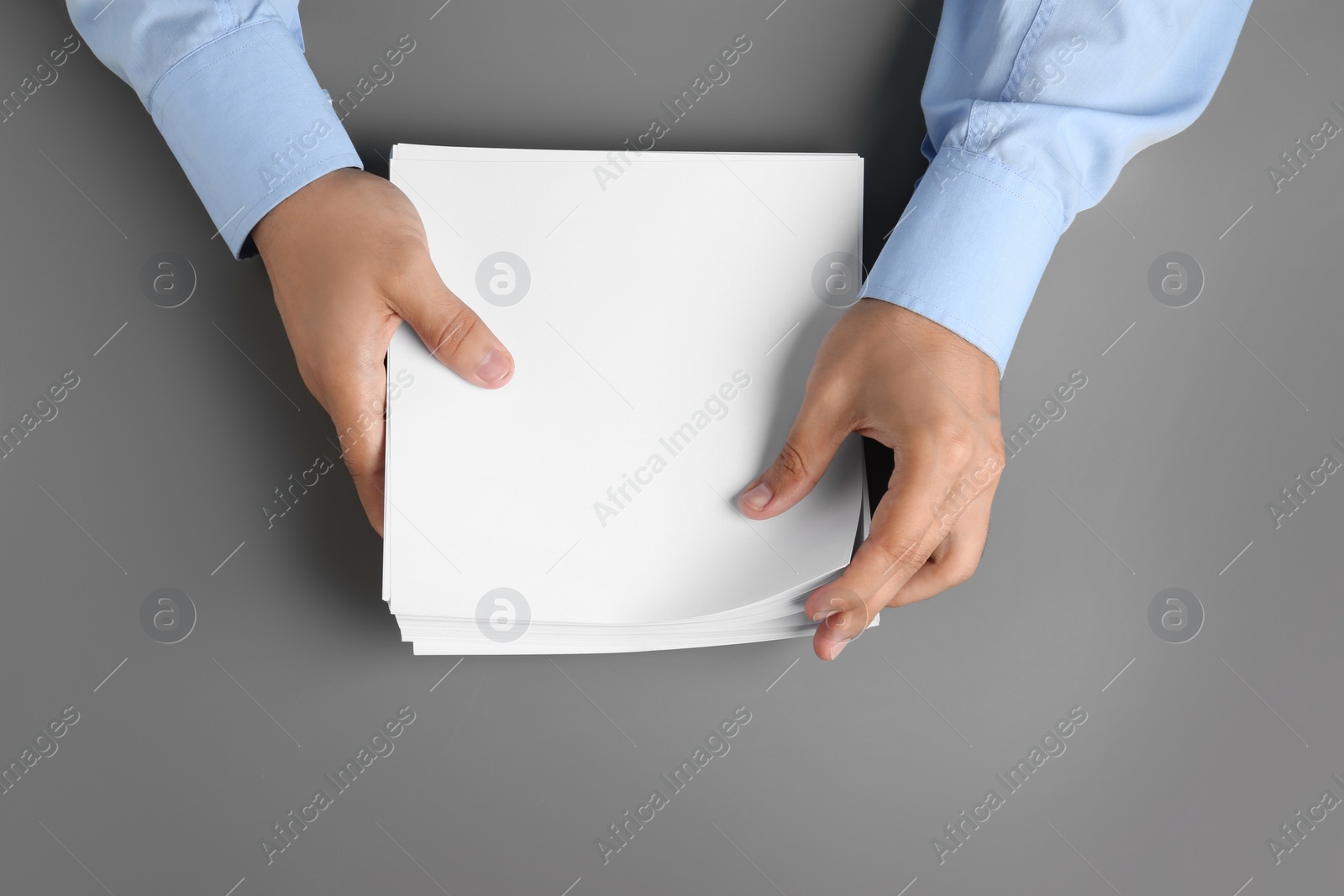 Photo of Man holding blank paper sheets for brochure at grey table, top view. Mock up