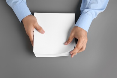 Man holding blank paper sheets for brochure at grey table, top view. Mock up