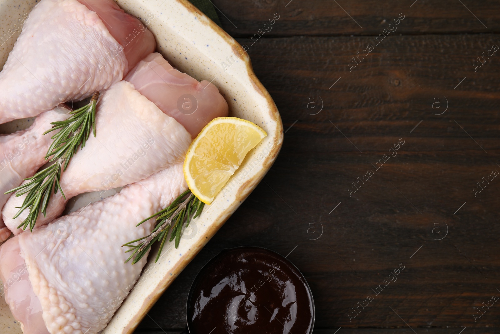 Photo of Marinade, raw chicken drumsticks, rosemary and lemon on wooden table, flat lay. Space for text