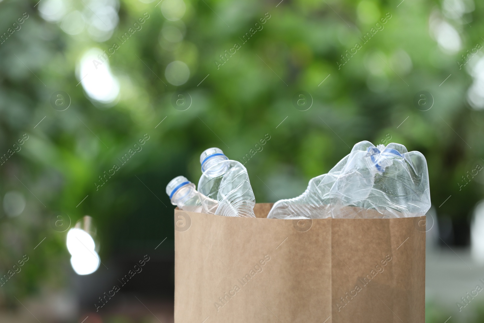 Photo of Used plastic bottles in paper bag on blurred background, space for text. Recycling problem