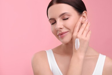 Photo of Beautiful woman with smear of body cream on her hand against pink background, space for text
