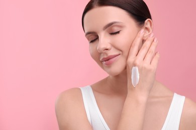 Beautiful woman with smear of body cream on her hand against pink background, space for text