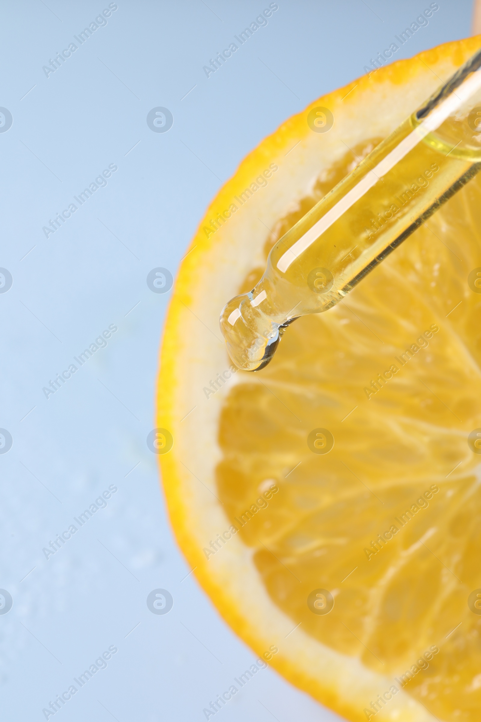 Photo of Dripping cosmetic serum from pipette onto orange slice against light blue background, top view