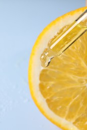 Dripping cosmetic serum from pipette onto orange slice against light blue background, top view