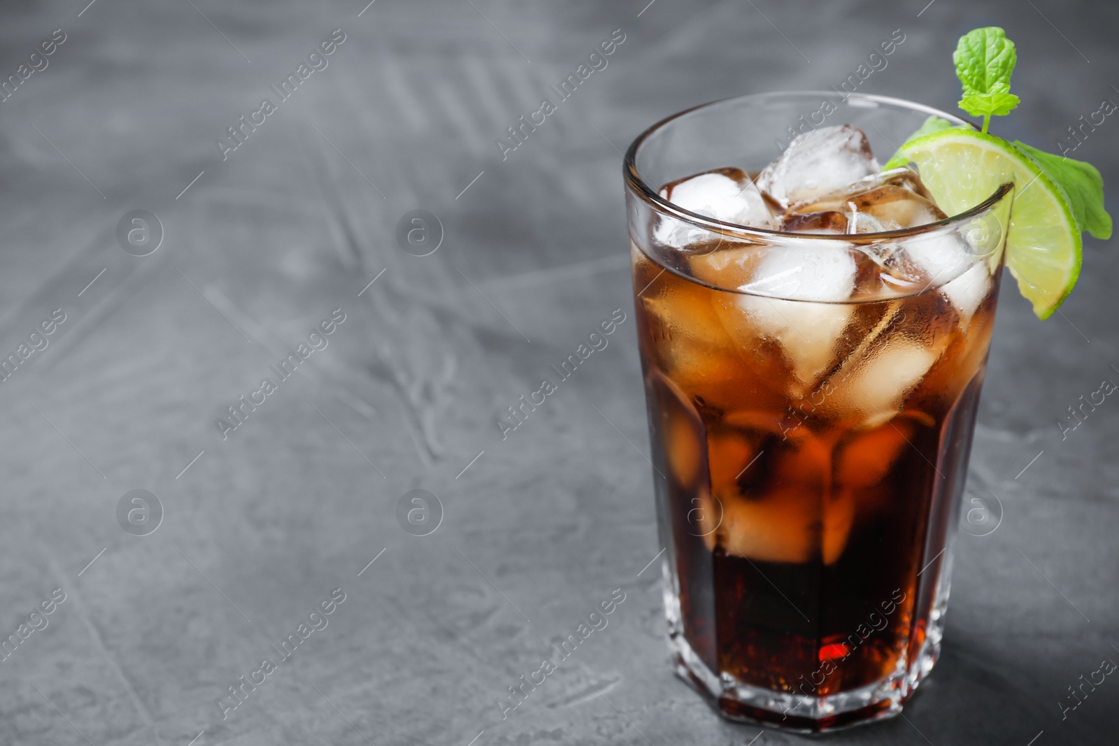 Photo of Glass of Rum and Cola cocktail on grey stone table, space for text