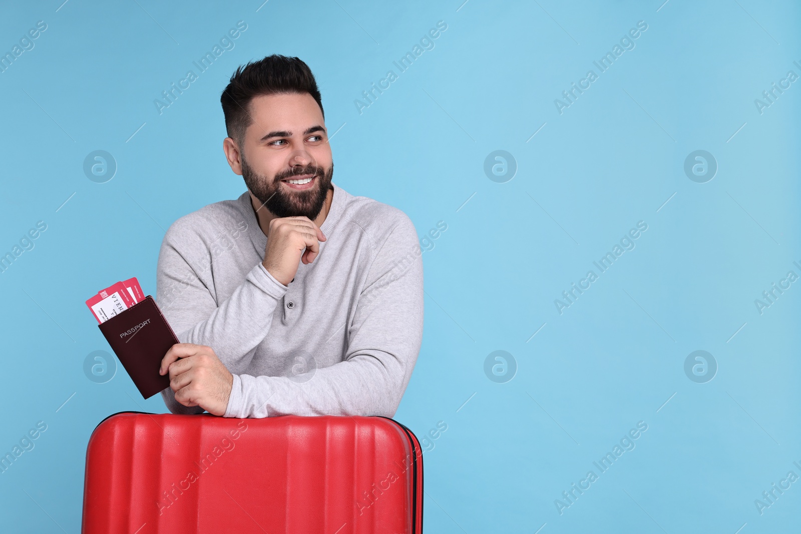 Photo of Smiling man with passport, tickets and suitcase on light blue background. Space for text