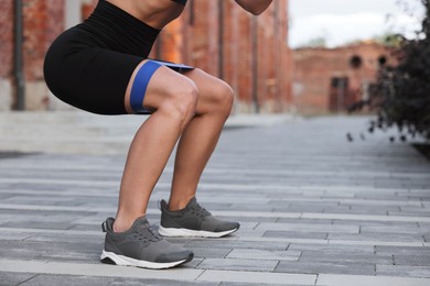 Photo of Woman doing squats with fitness elastic band outdoors, closeup