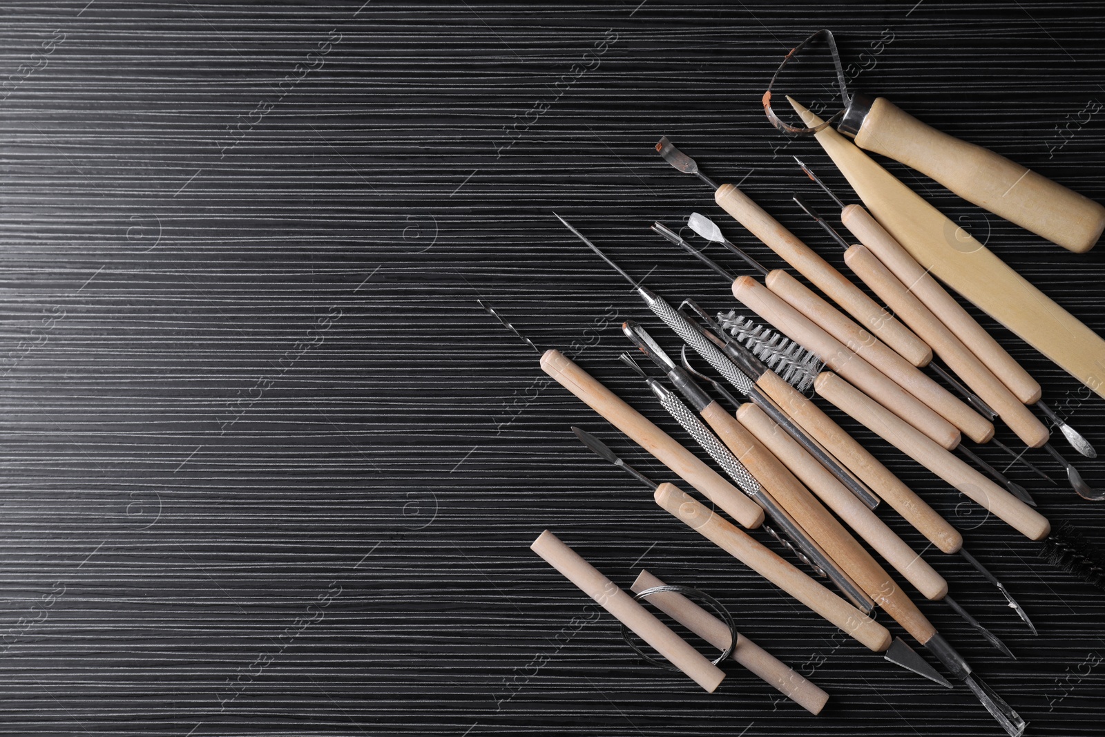 Photo of Clay and set of modeling tools on dark gray wooden table, flat lay. Space for text