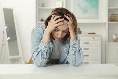 Photo of Sad young woman sitting at white table in room