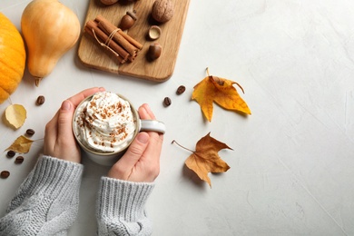 Woman with cup of tasty pumpkin spice latte at light table, top view. Space for text