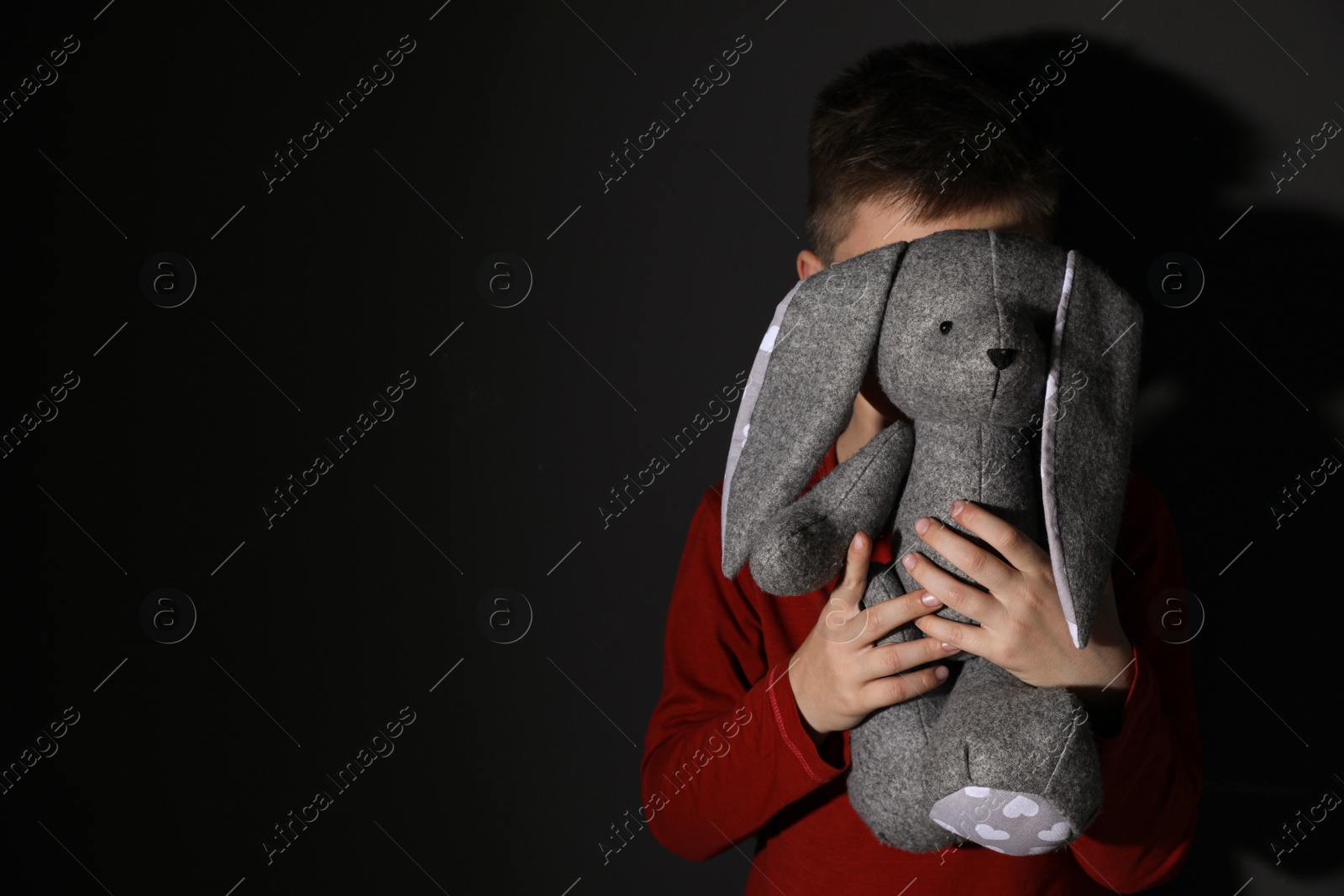 Photo of Little boy with toy near black wall, space for text. Domestic violence concept