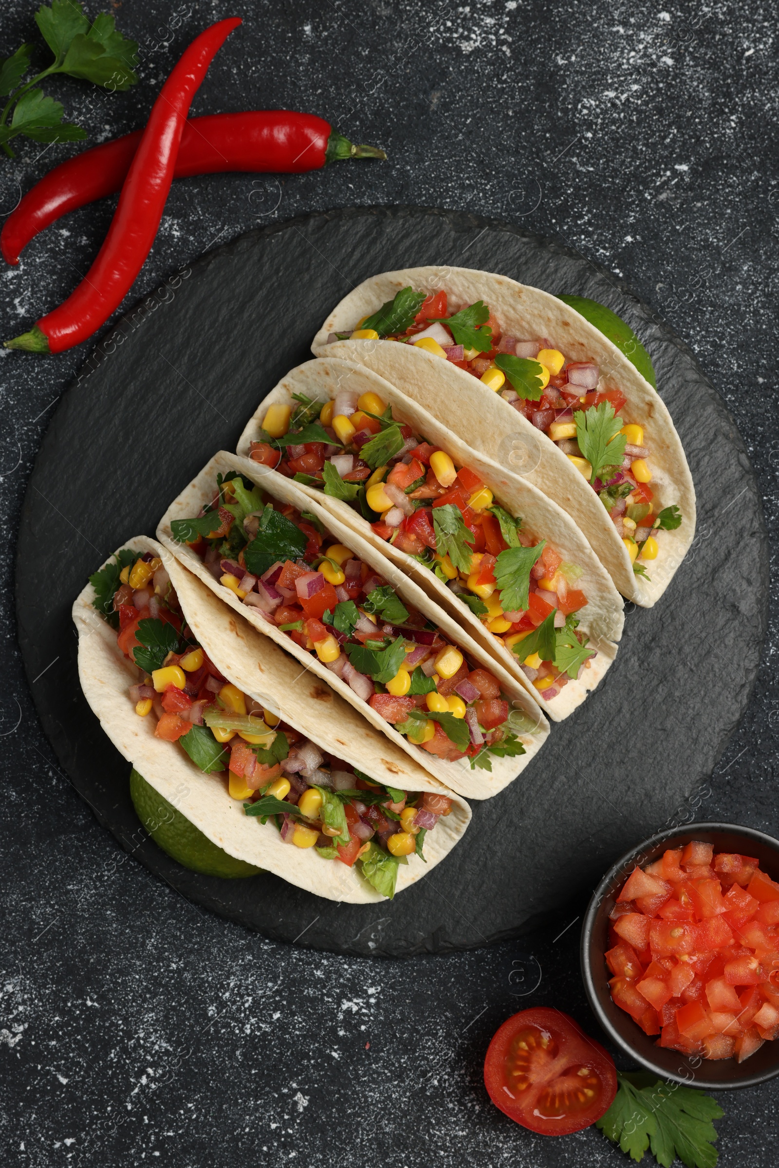 Photo of Tasty tacos with vegetables on black textured table, flat lay