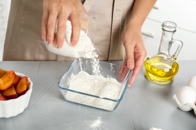 Photo of Woman pouring flour into bowl at light grey table, closeup. Cooking of delicious cake