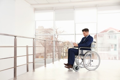 Photo of Young businessman in wheelchair using tablet near window indoors