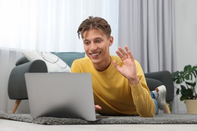 Happy young man having video chat via laptop on carpet indoors
