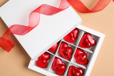 Photo of Beautiful heart shaped chocolate candies in box on beige background, flat lay