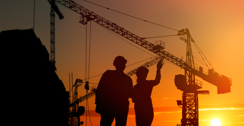 Image of Silhouettes of engineers near construction site at sunrise