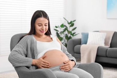 Beautiful pregnant woman sitting in armchair at home