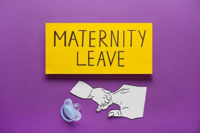 Photo of Note with words Maternity Leave, baby pacifier and paper cutout of hands on purple background, flat lay
