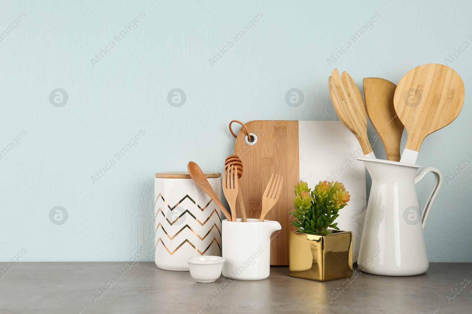 Photo of Potted plant and set of kitchenware on grey table near light wall, space for text. Modern interior design