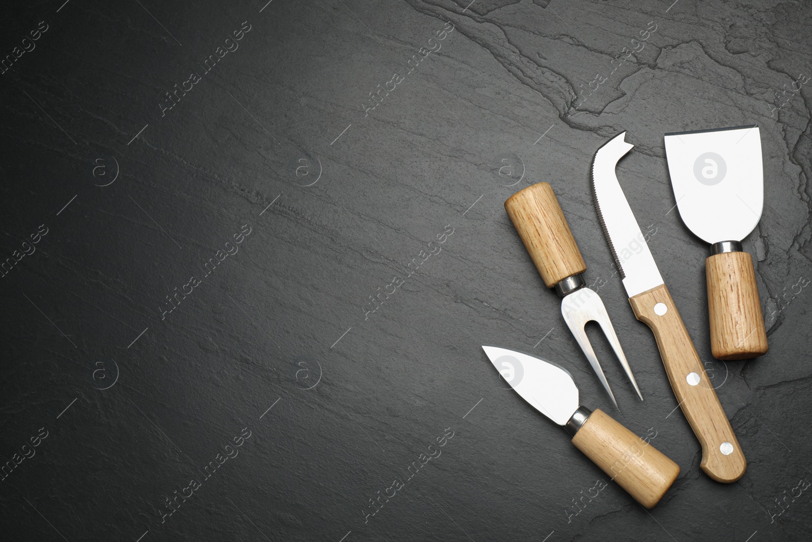 Photo of Cheese knives and fork on black stone table, flat lay. Space for text