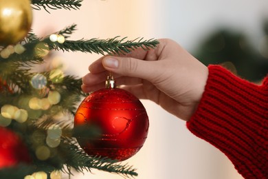 Photo of Woman decorating Christmas tree with red festive ball on light background, closeup