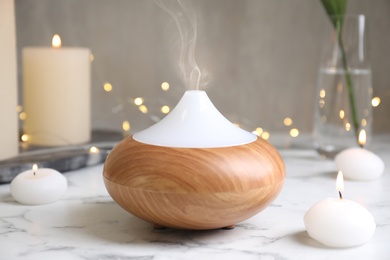 Photo of Aroma oil diffuser and burning candles on white marble table