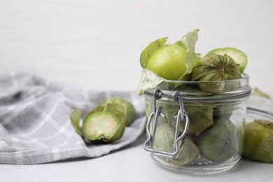 Photo of Fresh green tomatillos with husk in glass jar on light table, space for text