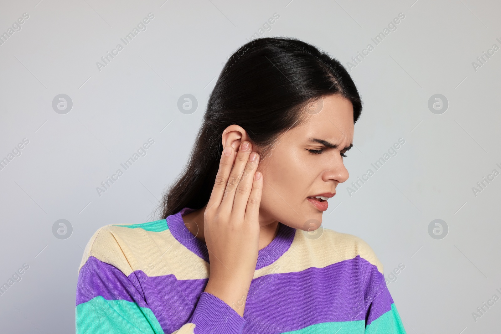 Photo of Young woman suffering from ear pain on light grey background