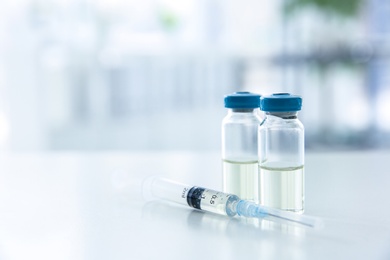 Photo of Vials and syringe with medicine on blurred background. Vaccination concept