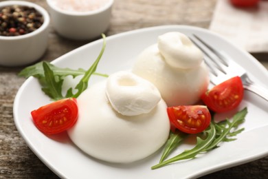 Photo of Delicious burrata cheese with arugula and tomato on wooden table, closeup