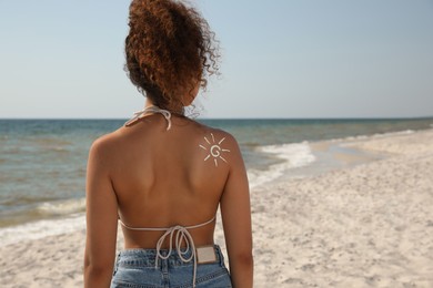 Photo of African American woman with sun protection cream on shoulder at beach, back view