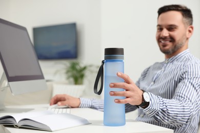 Photo of Man taking transparent plastic bottle of water while working in office, focus on hand