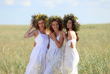 Young women wearing wreaths made of beautiful flowers in field on sunny day