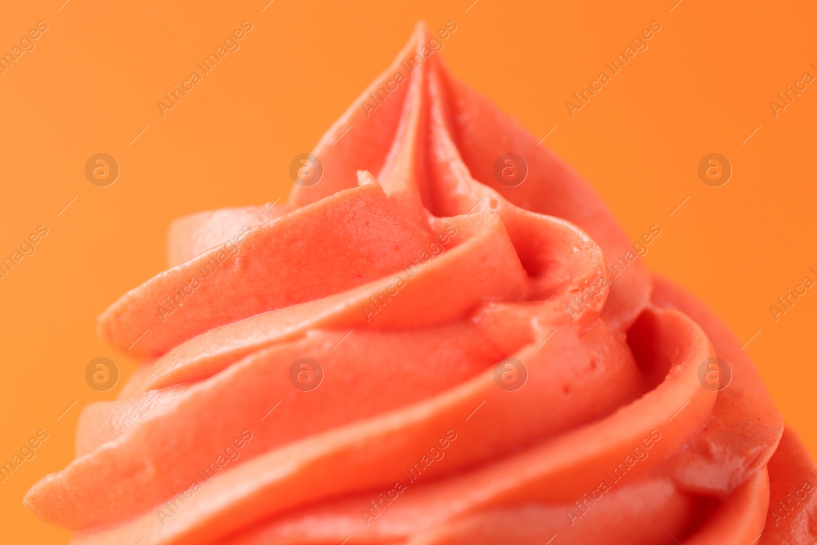 Photo of Delicious cupcake with bright cream on orange background, closeup