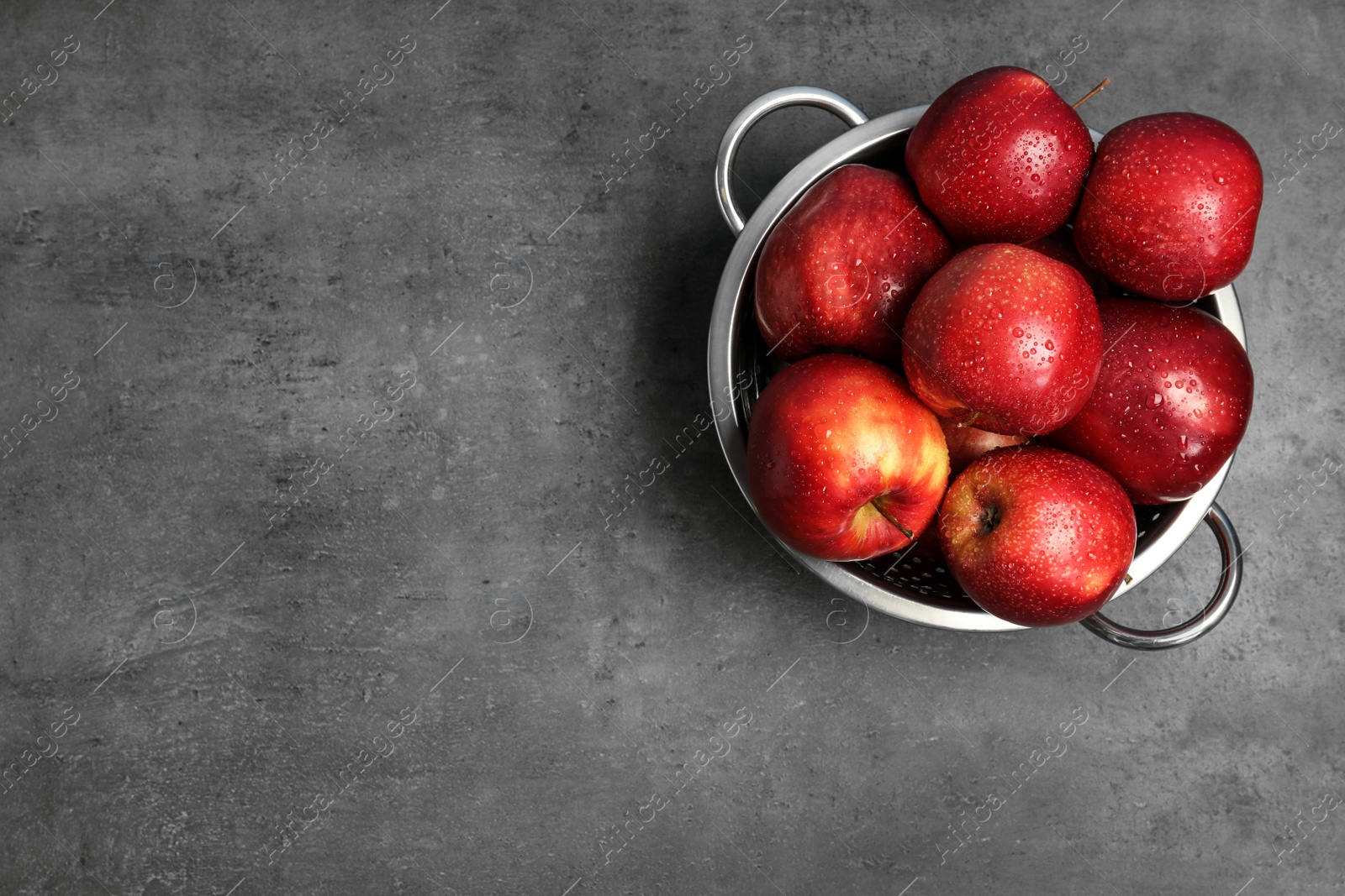 Photo of Juicy red apples in colander and space for text on grey background, top view