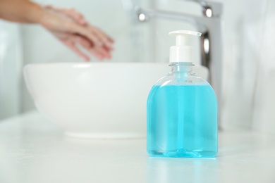 Photo of Bottle of antibacterial soap and blurred woman washing hands on background. Personal hygiene during COVID-19 pandemic