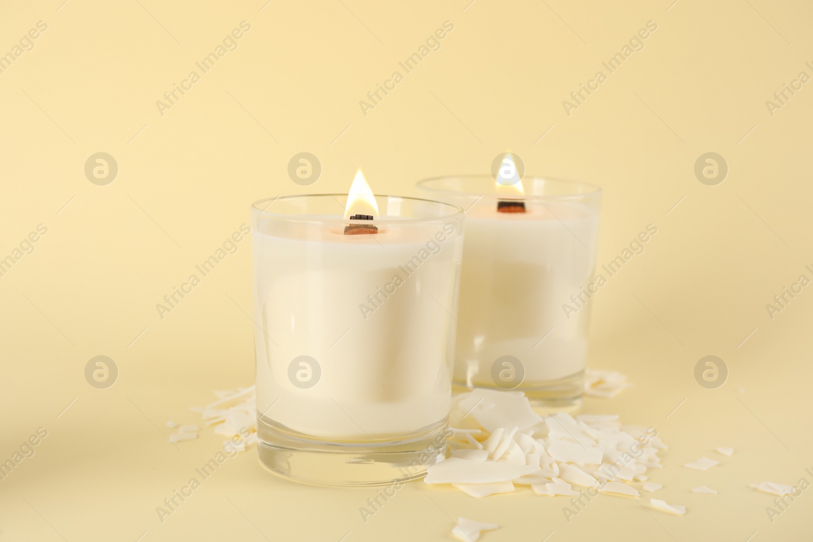 Photo of Burning soy candles and wax flakes on beige background