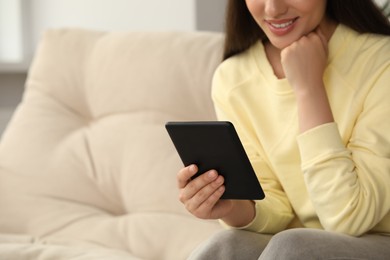Photo of Young woman using e-book reader on sofa at home, closeup. Space for text