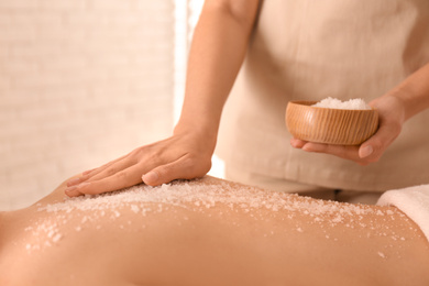 Photo of Young woman having body scrubbing procedure with sea salt in spa salon, closeup