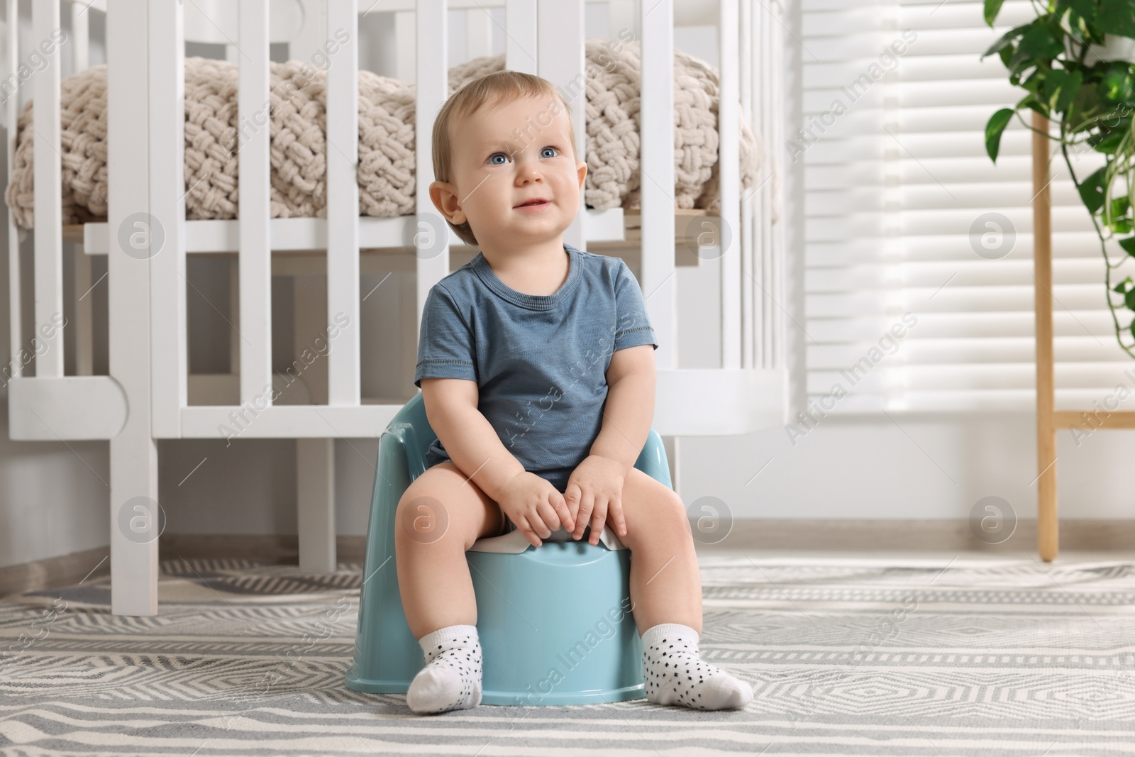 Photo of Little child sitting on plastic baby potty indoors. Space for text