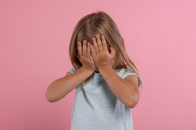 Resentful girl covering face with hands on pink background