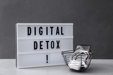 Photo of Trash bin of different gadgets and lightbox with words DIGITAL DETOX on light grey table
