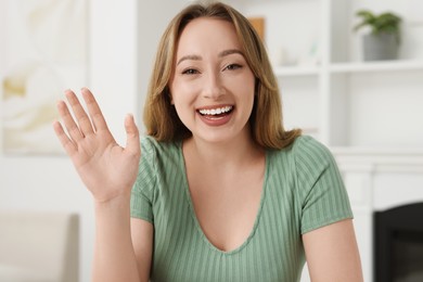 Photo of Young woman waving hello during video chat at home, view from webcam